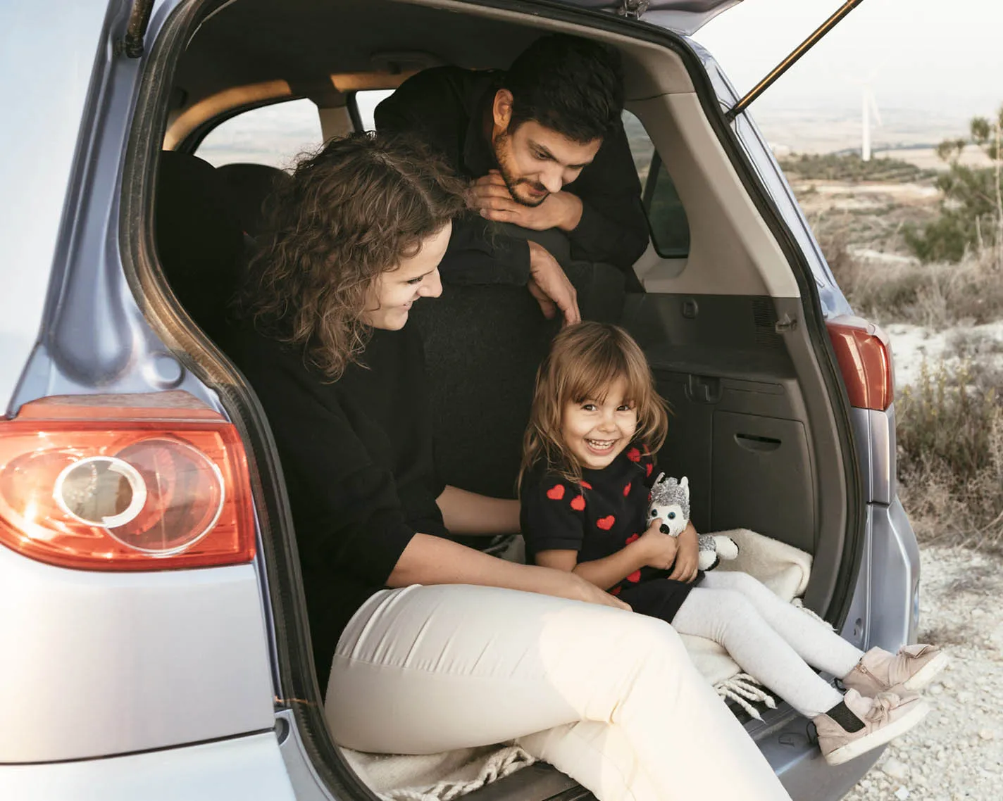Mother, father and young girl sitting in the boot of their car in a countryside location