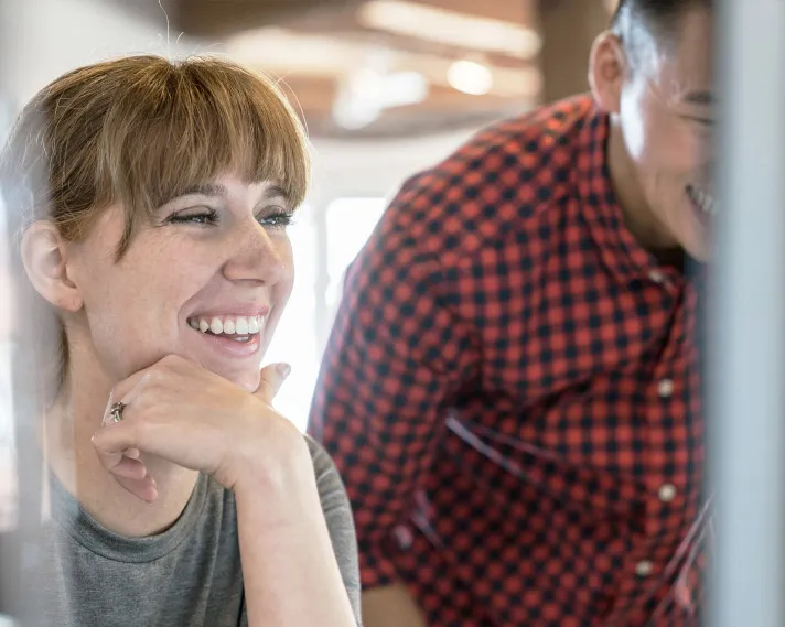 Woman with a fringe looking at a computer screen alongside a male colleague