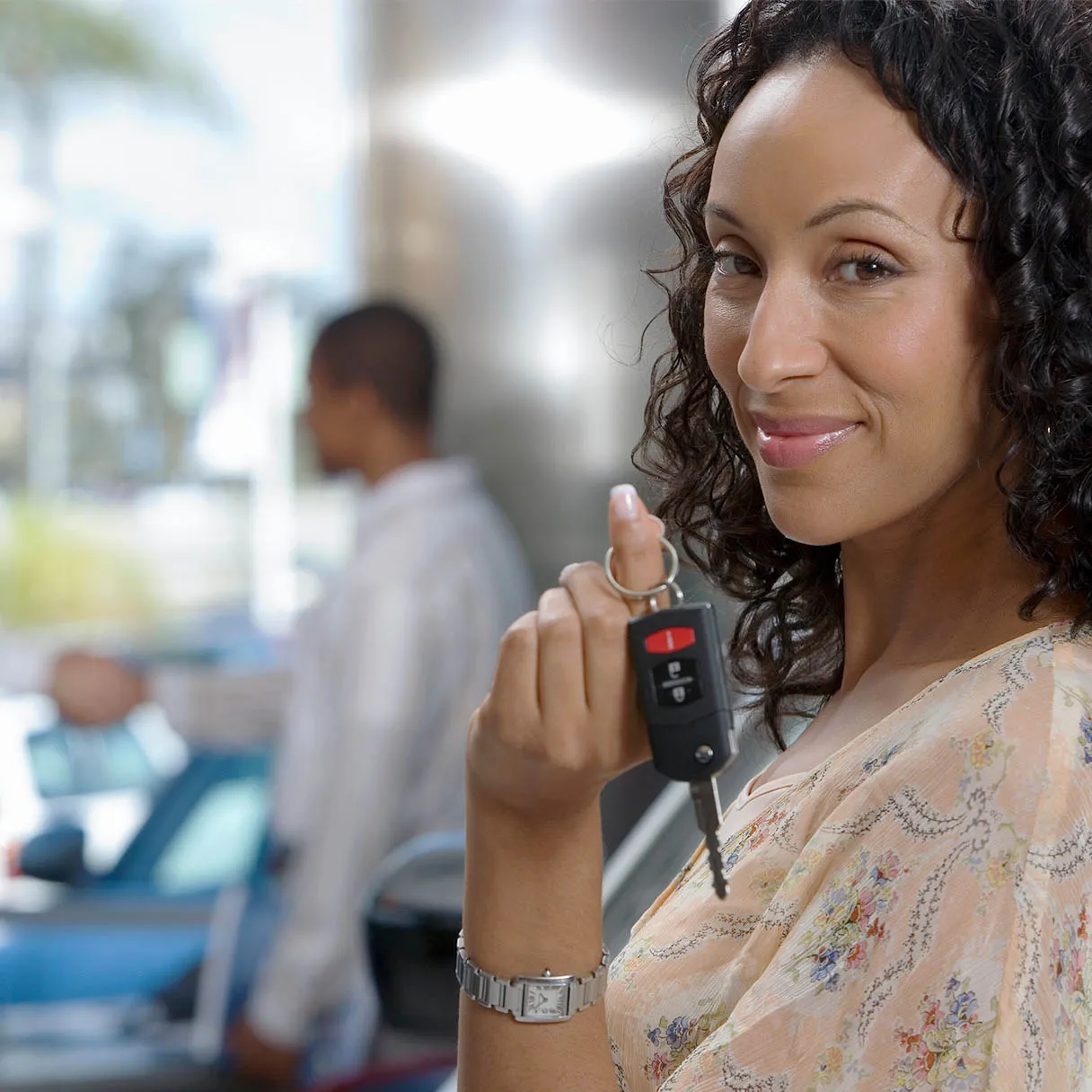 Woman at an auto dealership holding up the key to a new car