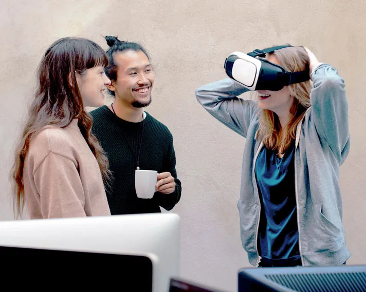 Woman putting on a virtual reality headset while two smiling friends watch her