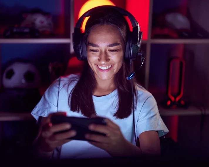 Woman with gaming headset on playing a mobile game in a dark room