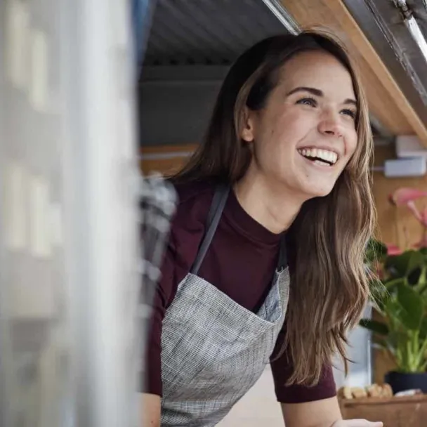 Person leaning out of a shop window, smiling as she engages with her community